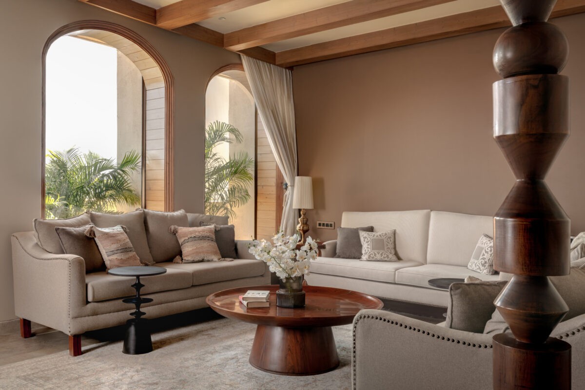 Cream sofas around a sculptural timber coffee table beneath exposed ceiling beams and tall arched windows at Still-Wood.
