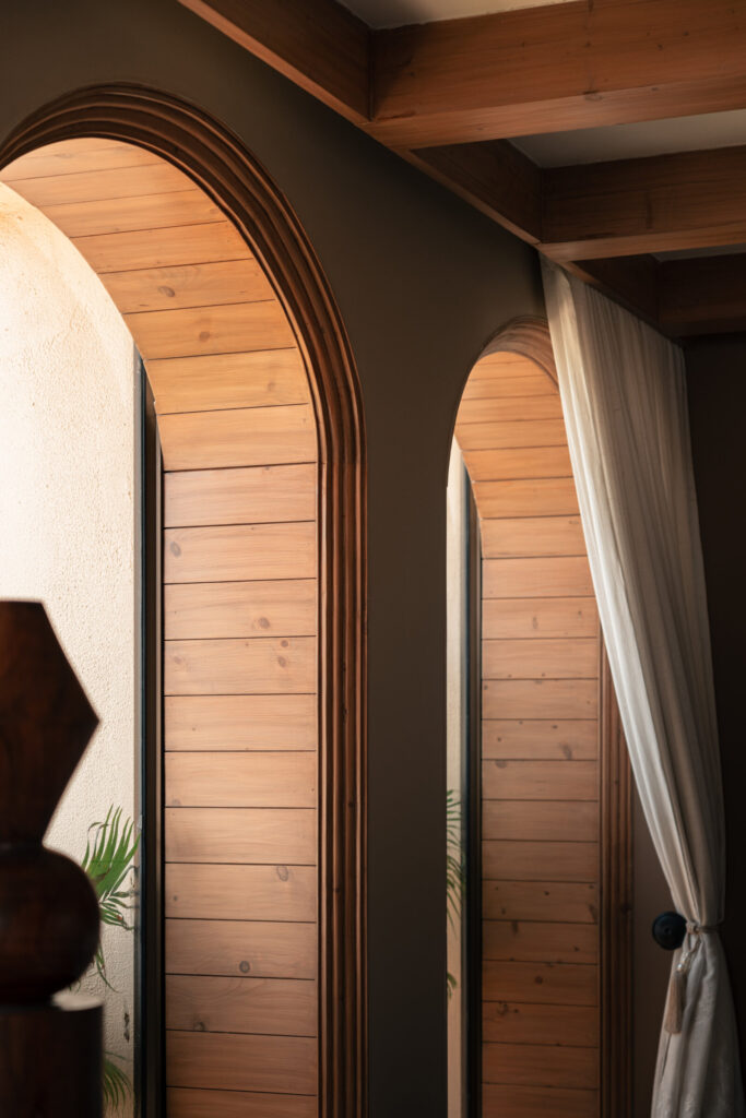 Paired arched windows with warm timber reveals beneath the exposed beams of the Still-Wood living room.