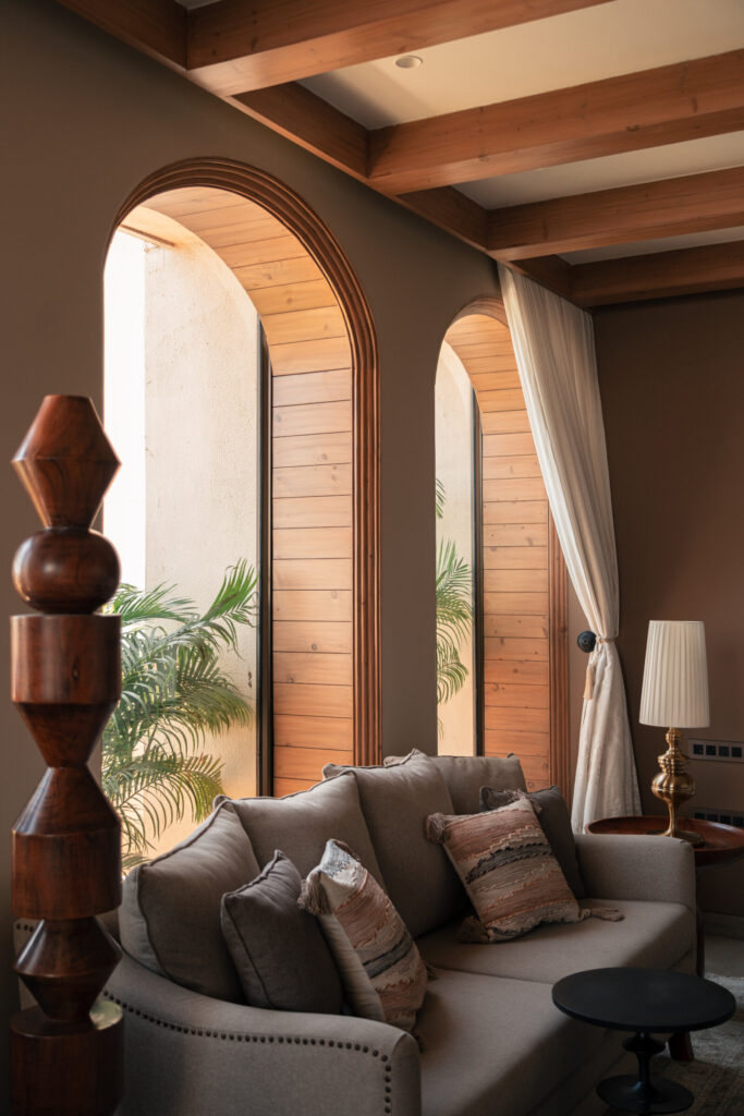 A cushioned sofa beside tall arched windows and a carved timber column in the Still-Wood living room.