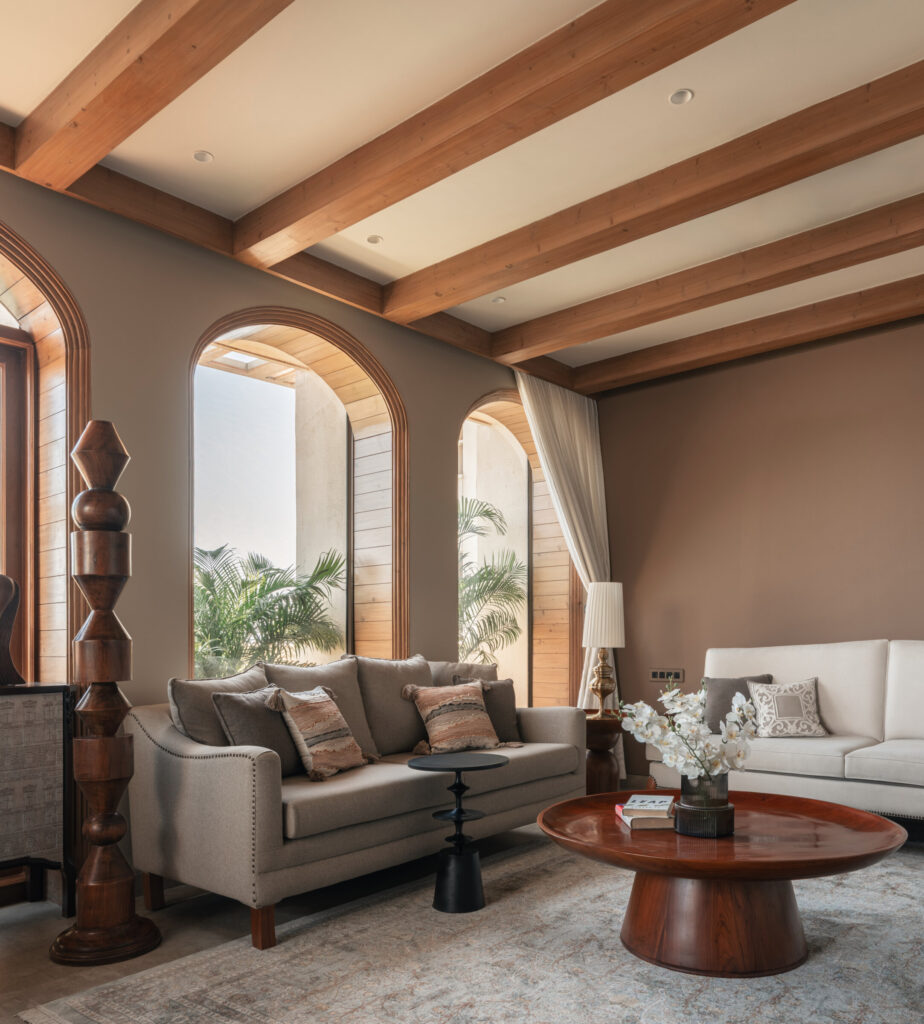 Still-Wood living room with exposed timber ceiling beams, arched windows, neutral sofas and a rounded coffee table.