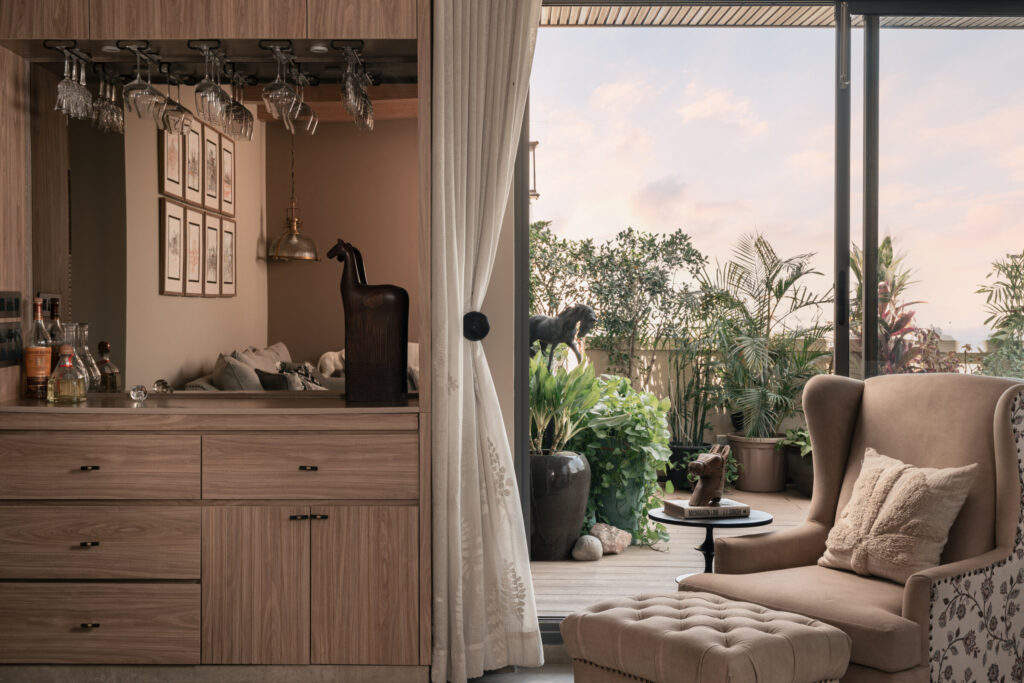 Timber cabinetry and a mirror beside a cushioned chair facing a planted terrace at Still-Wood.