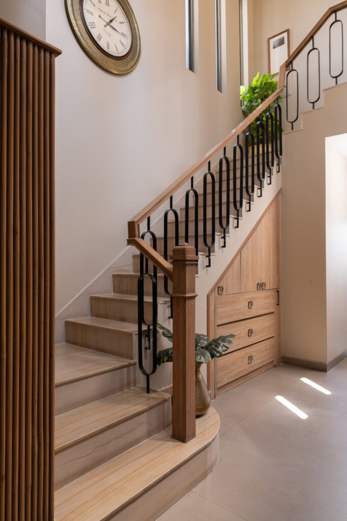 A pale stone staircase with a timber handrail and dark balusters beside framed artwork and a wall clock at Still-Wood.