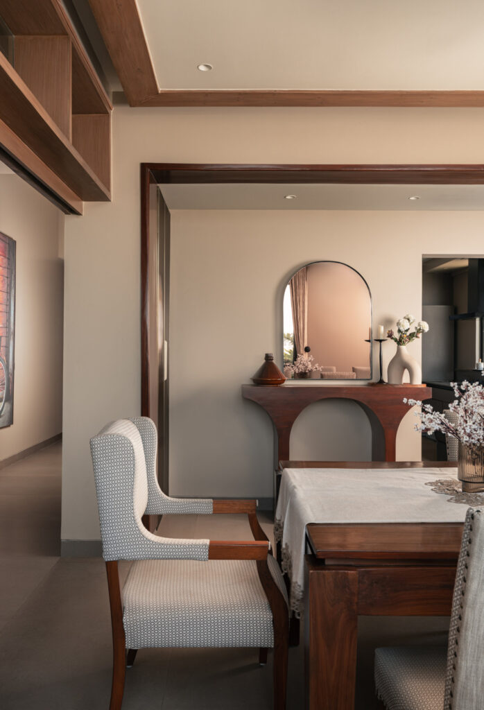 Upholstered chairs around a timber dining table, with a sculptural console and arched mirror beyond at Still-Wood.