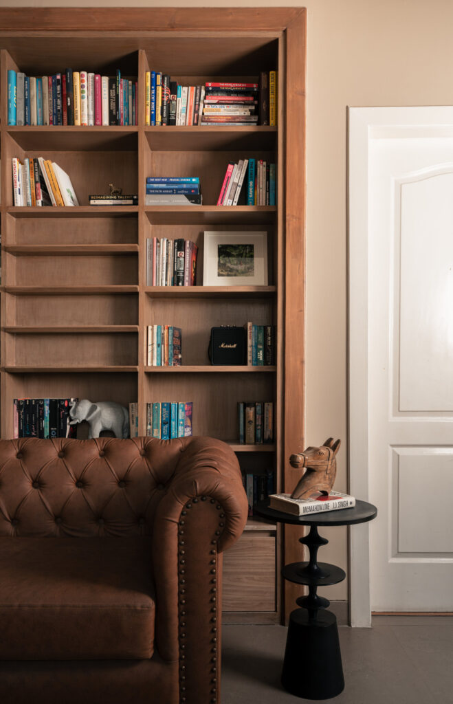 Built-in timber bookshelves filled with books above a tufted leather chair and a small side table at Still-Wood.