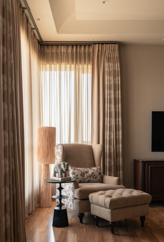 A cushioned armchair and matching ottoman set beside floor-length curtains and softly filtered daylight at Still-Wood.