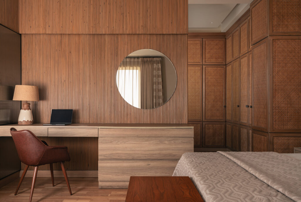 A timber dressing desk and round mirror beside paneled wardrobes and the bed in a Still-Wood bedroom.