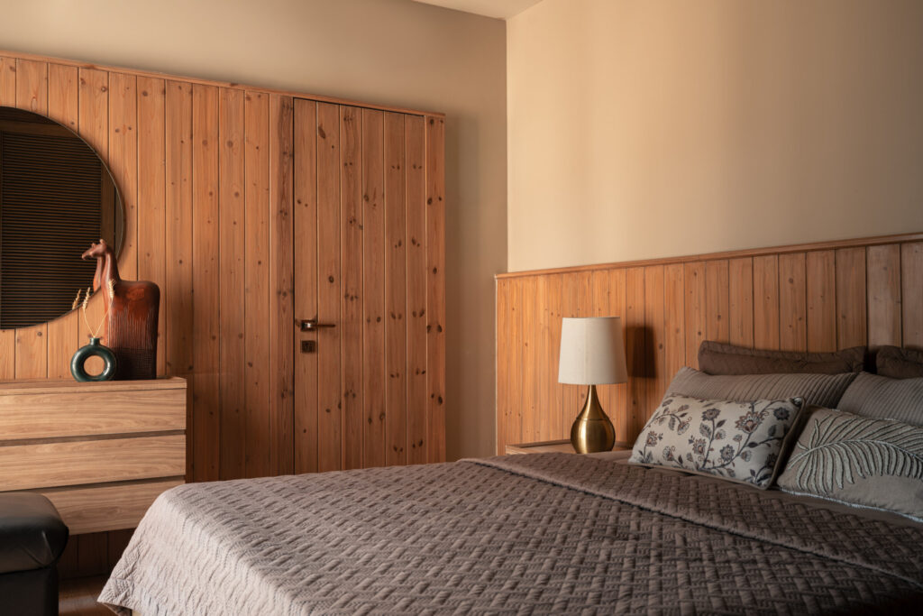 A bed with a quilted cover and timber headboard beside matching wardrobes and a round dressing mirror at Still-Wood.