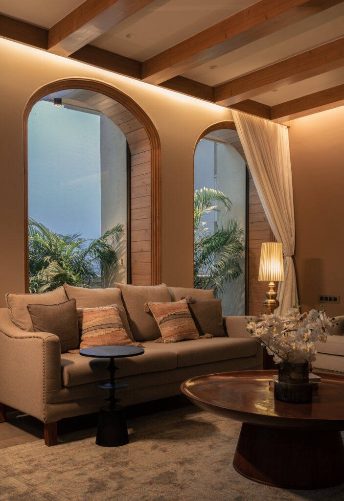 Warm evening lighting across the Still-Wood living room, with arched windows, a sofa and rounded coffee table.