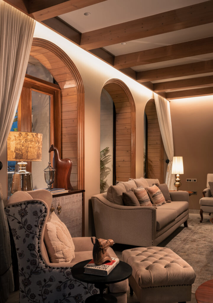 Patterned lounge chairs and a cushioned sofa beneath exposed timber beams and softly lit arched windows at Still-Wood.